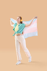 Young woman in headphones with transgender flag on beige background