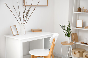 Workplace with willow branches in vase and frame near light wall