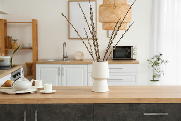 Vase with willow branches and breakfast on counter in kitchen
