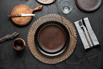 Beautiful table setting with wooden plates and tree branch on dark background