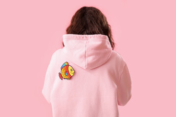 Teenage girl with paper fish on pink background, back view. April Fools' Day celebration
