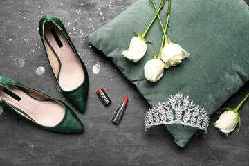 Beautiful tiara, pillow, roses, lipstick and heels on dark background. Prom concept