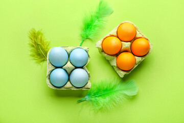Cardboard holders with painted Easter eggs and feathers on green background