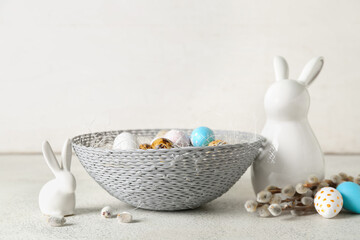 Bowl with Easter eggs, ceramic bunnies and willow branches on light table