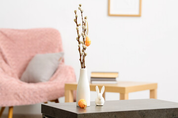 Vase with willow branches, Easter eggs and ceramic bunny on table in room