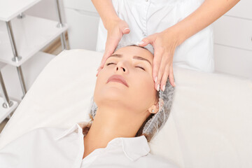 Cosmetologist massages woman face skin after rubbing moisturizing cream for rejuvenation, anti...