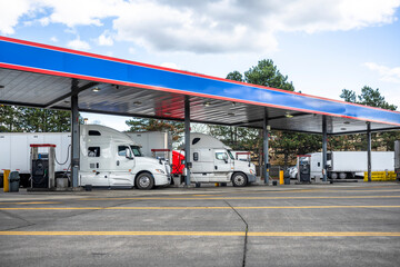 Big rigs semi trucks with semi trailers fuel trucks tanks with diesel on the truck stop gas station