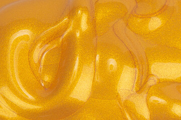 Texture of a golden cosmetic product. Golden acrylic paint close-up. Spreading gold