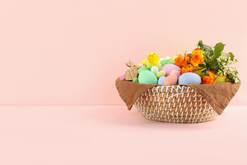 Wicker basket with Easter eggs, decor and flowers on color background
