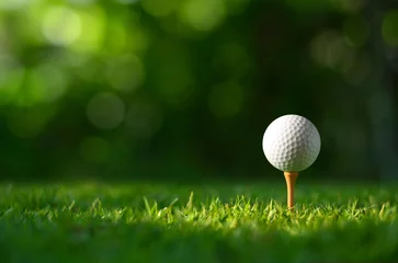 Zelfklevend Fotobehang Close-up golf ball on tee with blur green bokeh background. © Paitoon