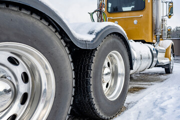 Day cab yellow big rig semi truck tractor with two driving axles and powerful wheels tires standing on the parking lot with winter snow and ice