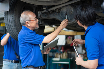 Senior Asian engineer teaching worker repair and maintenance car rear axle of the car. Group technician in uniform checking and servicing vehicle in garage.