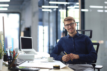 Handsome male architect looking at camera and smiling while sitting in the office.