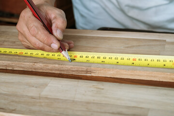 Carpenter using a measuring tape and mark a cut line with pencil on a wood board.DIY maker and woodworking concept. selective focus