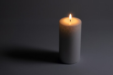 Fototapeta na wymiar A lighted white wax candle burning isolated on dark white background with low light shadow. 