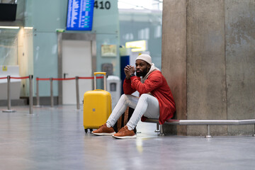 Sad African American man upset at airport his flight is delayed. Depressed traveler male waiting...