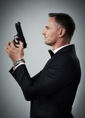 Agent man, profile and gun with suit for mission, justice or espionage by grey studio background....