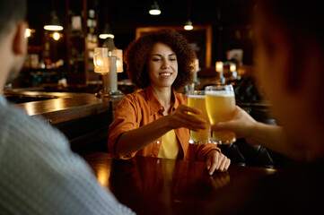 Friends drinking beer cheering glasses sitting at table in sport bar