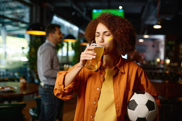 Young girl football fan drinking beer while rest in sports bar with friends