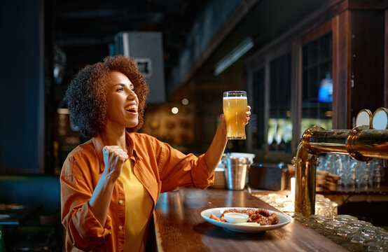 Young woman cheering for favorite team watching match in sports bar