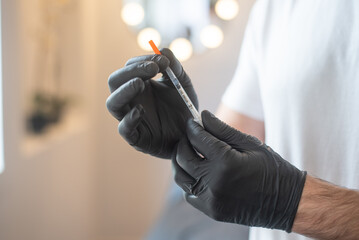 Man's hands in black gloves hold syringe for cosmetic injections. space for copy text. Person in with t-shirt. Make Vaccinations. Beaty salon