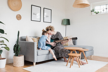 mother and daughter cuddling whilst playing the guitar at home