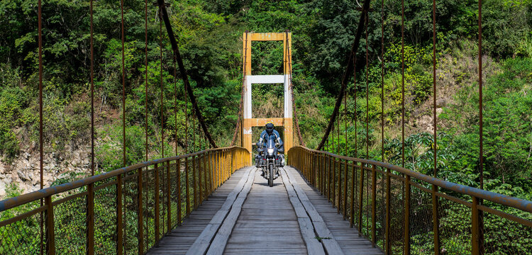 Man driving touring motorbike on suspension bridge in Peru