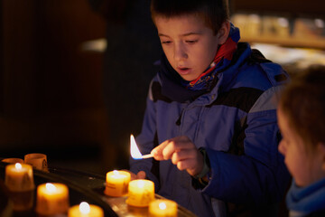 child with a match is going to light a candle inside a church