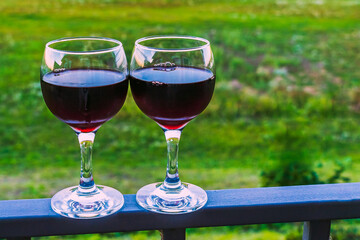 Two glasses with red wine on the railing of the veranda in the garden