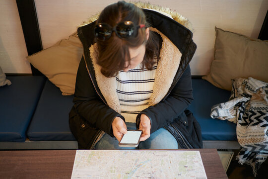 woman sits looking at her phone in front of a tourist map