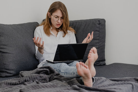 Attractive Young Woman Working from Home - Female Entrepreneur Sitting on sofa with Laptop Computer and Checking Cell Phone from Comfort of Home