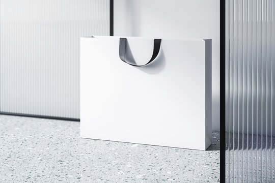 Perspective view on blank white paper shopping bag with place for your brand name or text on light concrete floor and light wall background, close up. 3D rendering, mockup