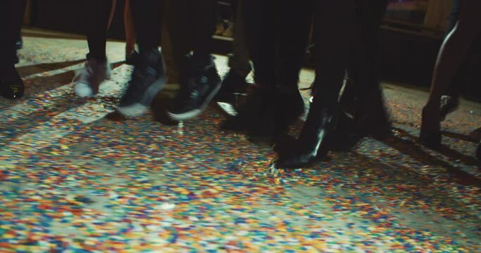 Cropped image of people's feet dancing on a floor covered with confetti