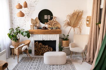Eco style living room interior with fireplace, wicker chair, tea table, indoor plant, wicker rug and baskets, books and round mirror on white wall.