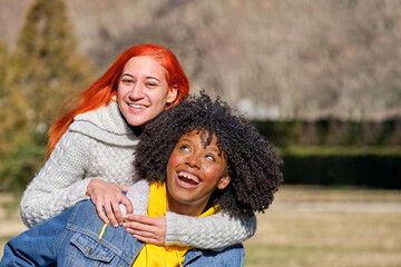 two friends, one climbs on the back of the other, having a good time in a park