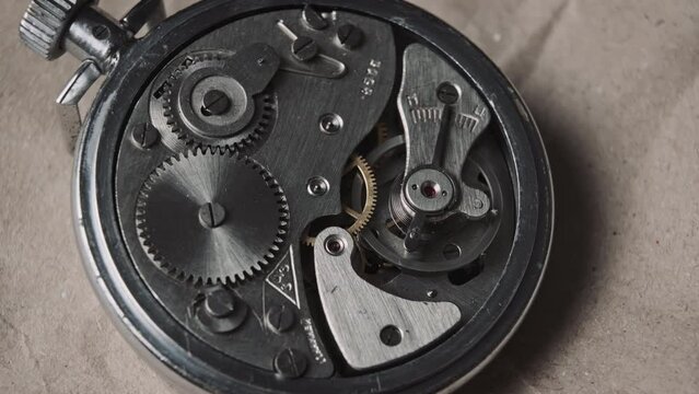 Clock mechanism rotates close-up. Vintage round stopwatch mechanism working in a macro. Old retro clockwork gears, cogwheels, and pendulum movement inside the ancient metal watch.