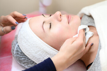 A woman cosmetologist washes a client with cotton wool and water,