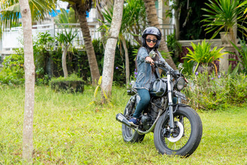 Pretty looking girl in a denim clothes sits on a black motorbike with a helmet