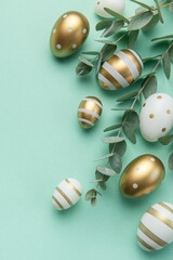 Easter eggs painted in gold and eucalyptus branches on a soft green background.