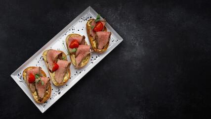 Bruschetta with meat, sauce and tomatoes, on a dark background