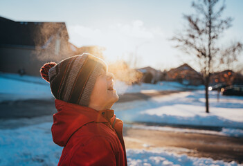 Boy in winter clothing laughing in frosty air on sunny winter day.