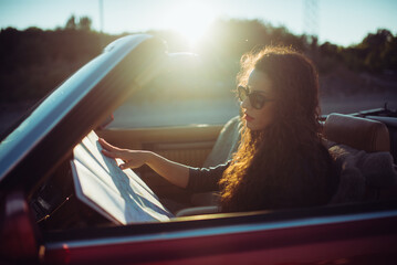 Woman with curly hair reading a map in the vintage car with suns