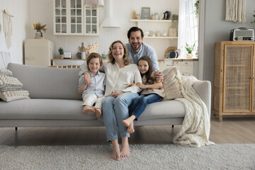 Joyful family couple and little son and daughter kids sitting on sofa, resting on comfortable couch...