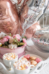 Flowers and sweets on white table and balloons on the white bed. Gift for Valentine's day or March 8 or Mother's Day or birthday