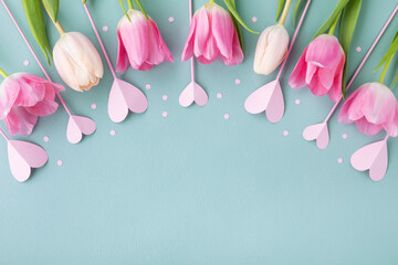 Bouquet of beautiful spring flowers and pink hearts on pastel blue table top view. Greeting card...