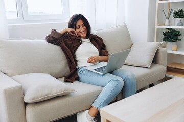 Obraz premium Woman freelancer on her day off sitting on the couch with a laptop at home and watching series and tv shows, smile