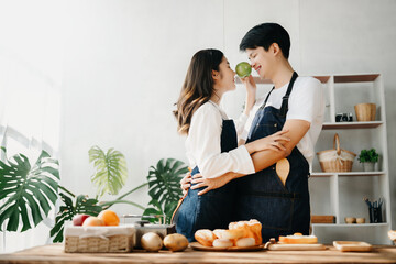 A man in the kitchen preparing a meal with Bread and fruit in cozy kitchen while his wife hugging him. sweet home.