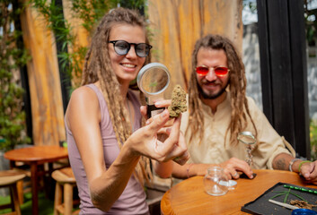 Hippie style couple examines under a magnifying glass the joints and buds of medical marijuana