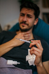 Man with a sore throat. The young Caucasian man sitting at home on a sofa, feeling sick, having a...