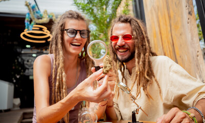 Hippie style couple examines under a magnifying glass the joints and buds of medical marijuana